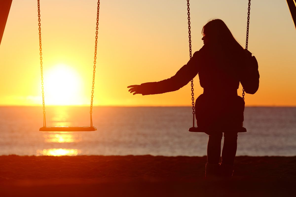 women on swing with empty swing beside her (sunset)
